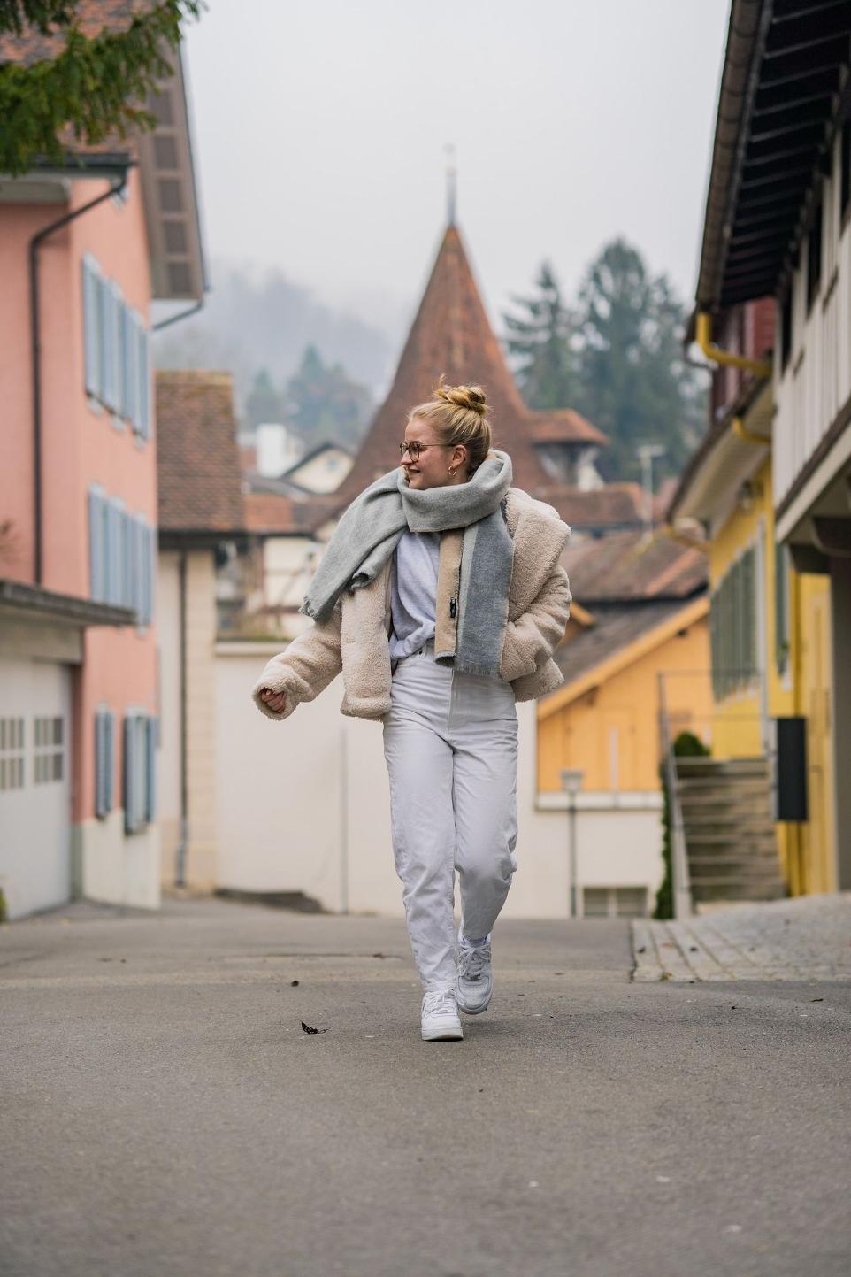 a woman walking down a street with a scarf around her neck